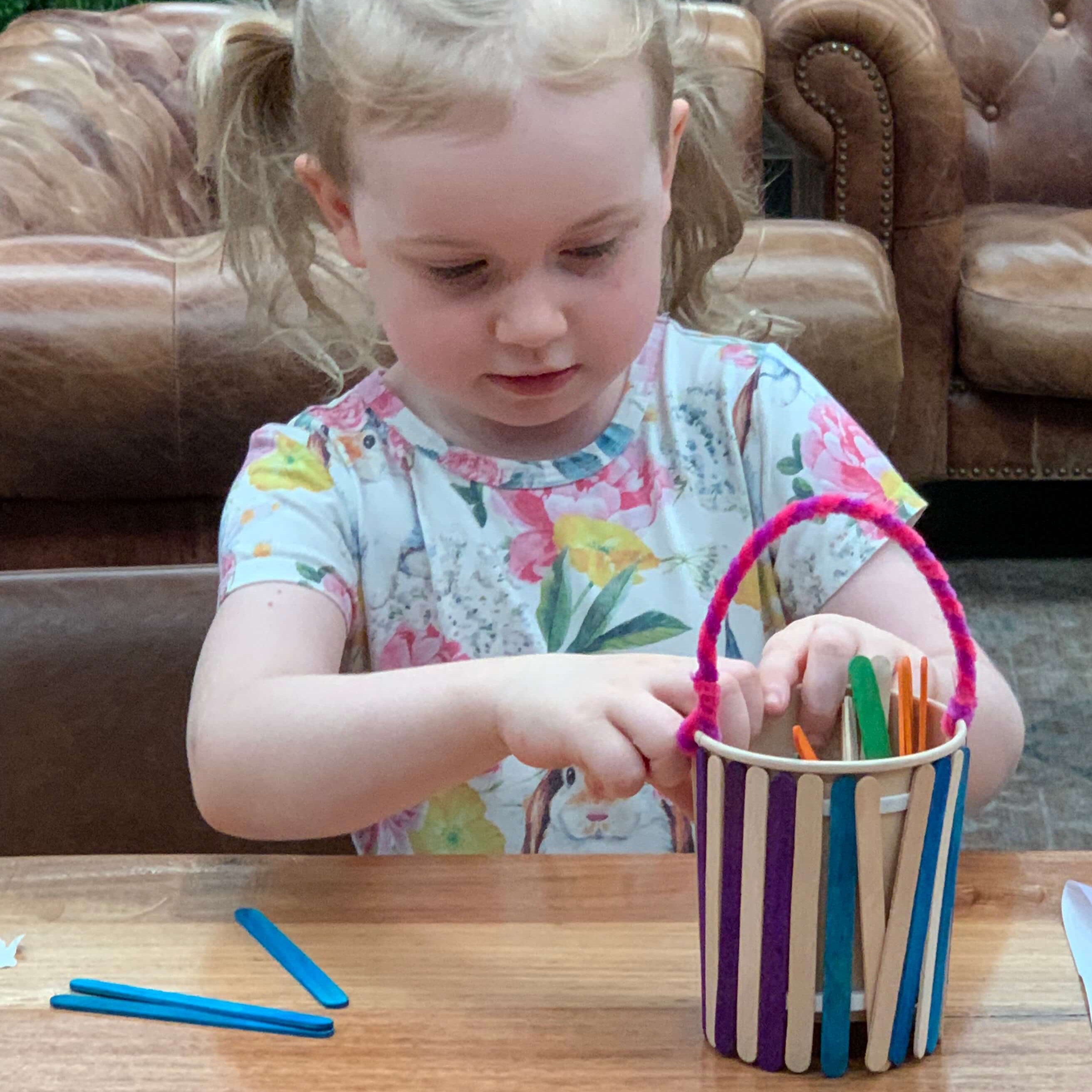 A girl is making a wooden basket on the table