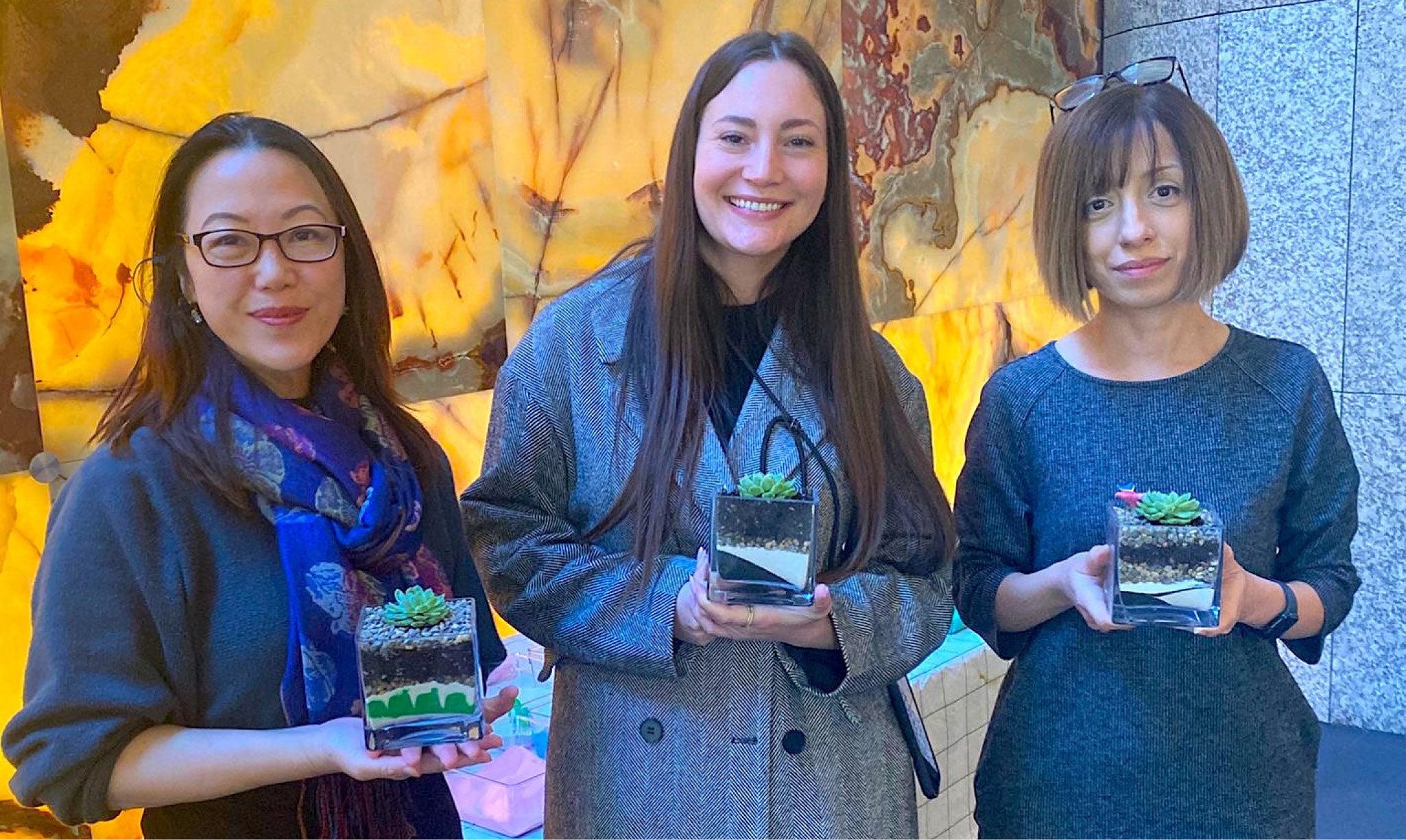 Three women holding sand and succulent terrariums.