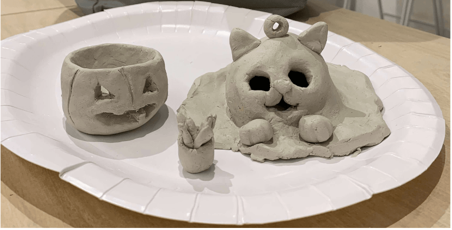 Three clay sculptures on a white paper plate: a cat, a mouse, and a pumpkin.