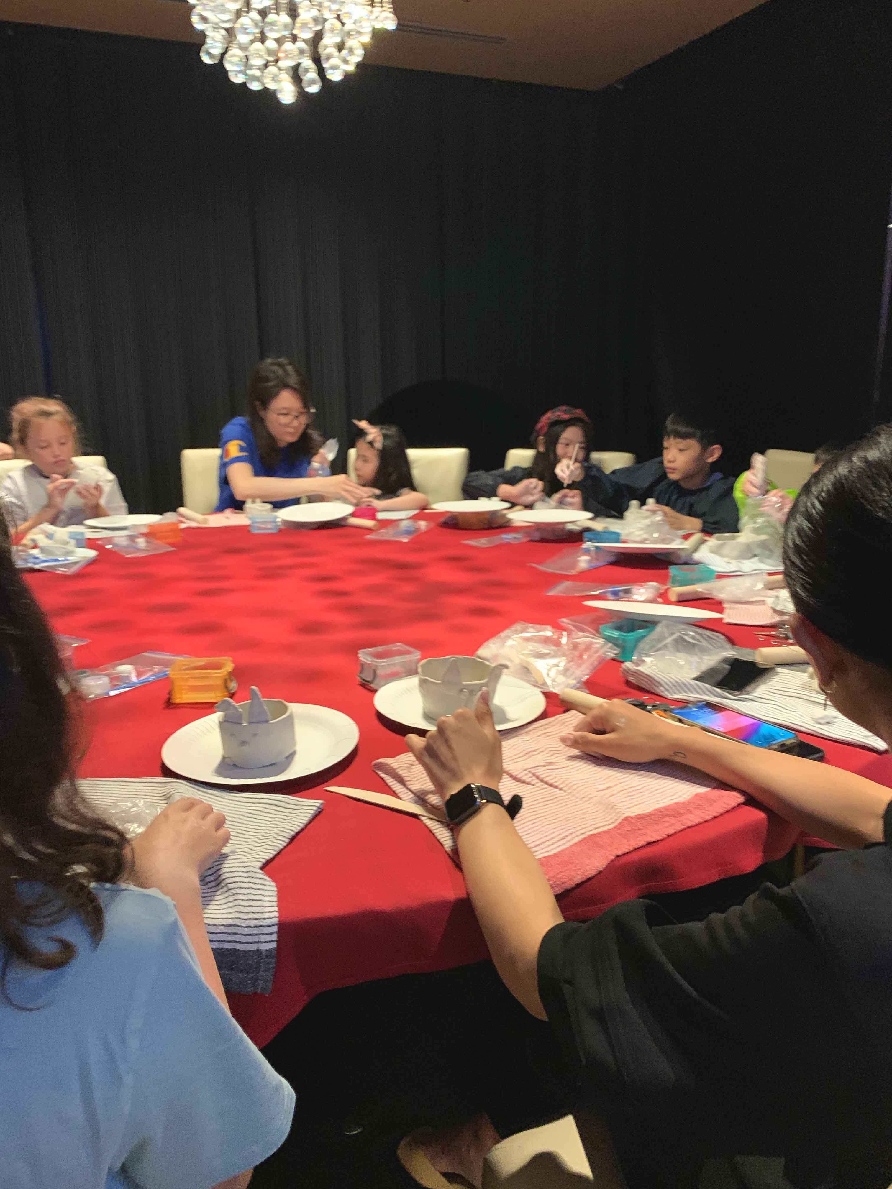 A group of people sitting around a table making rabbit vessel from air dry clay.