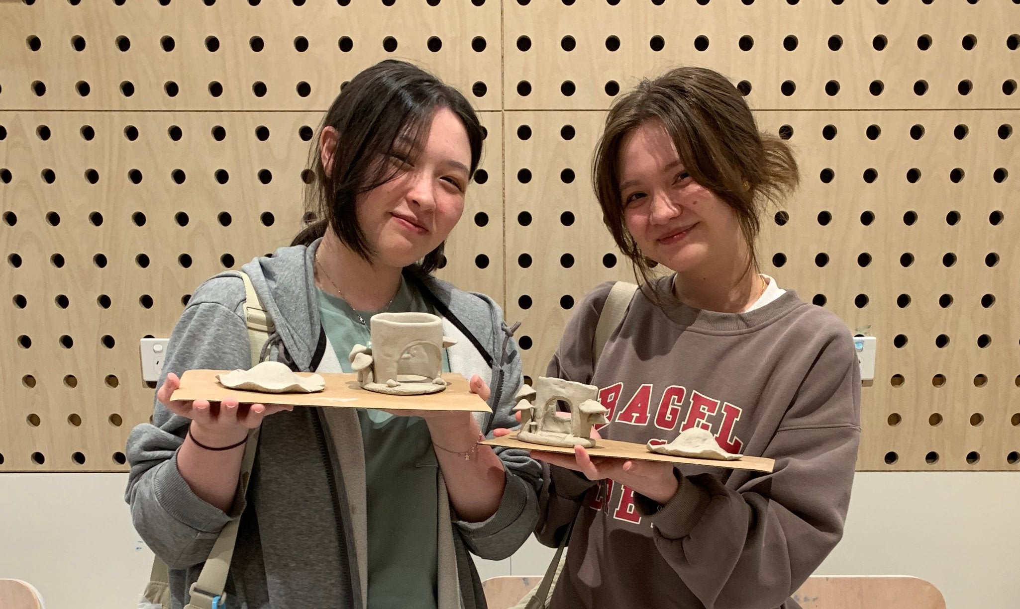 Two people holding fairy mushroom house sculpture.