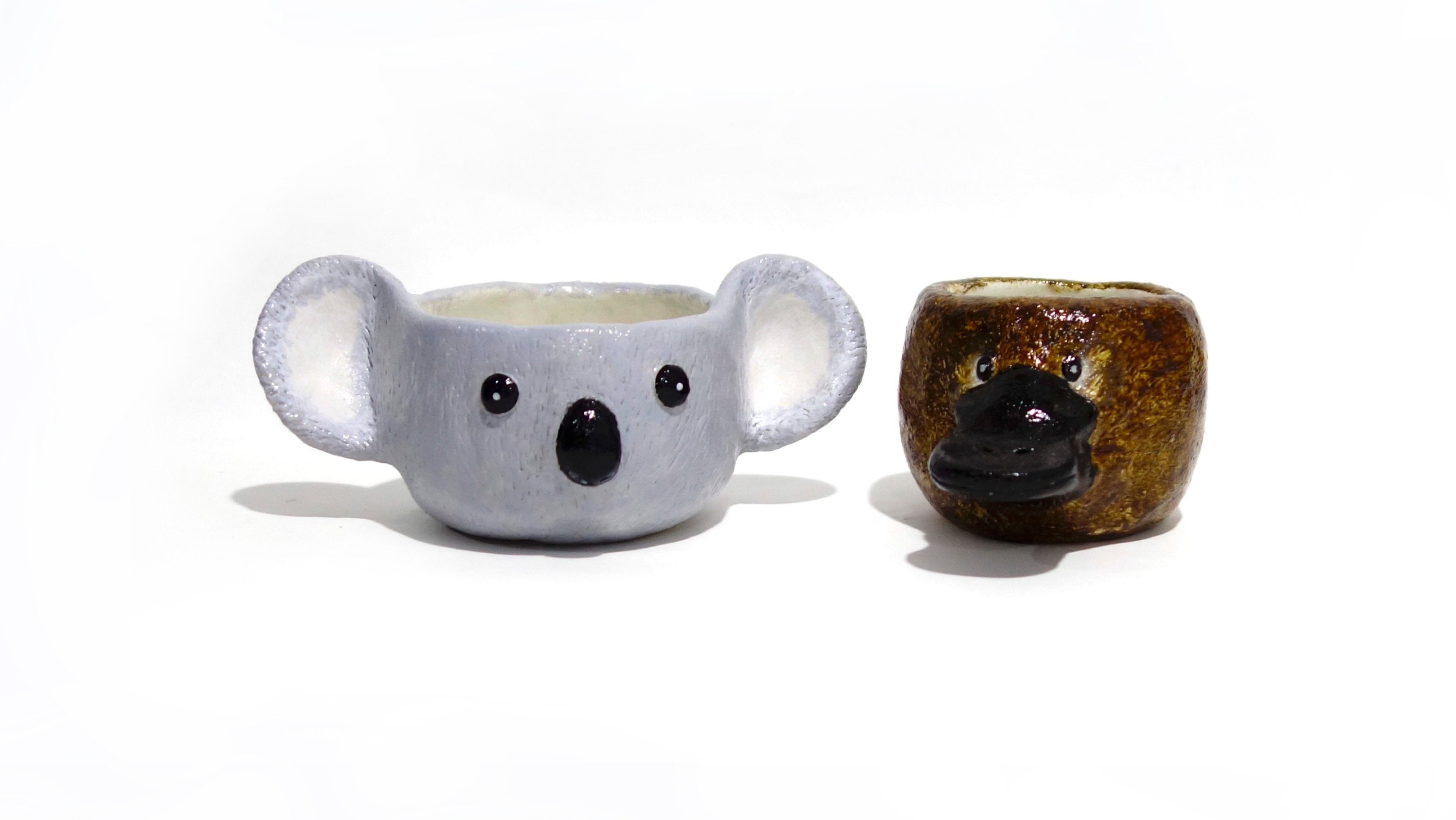 Two small planters shaped like a koala and platypus from air dry clay.