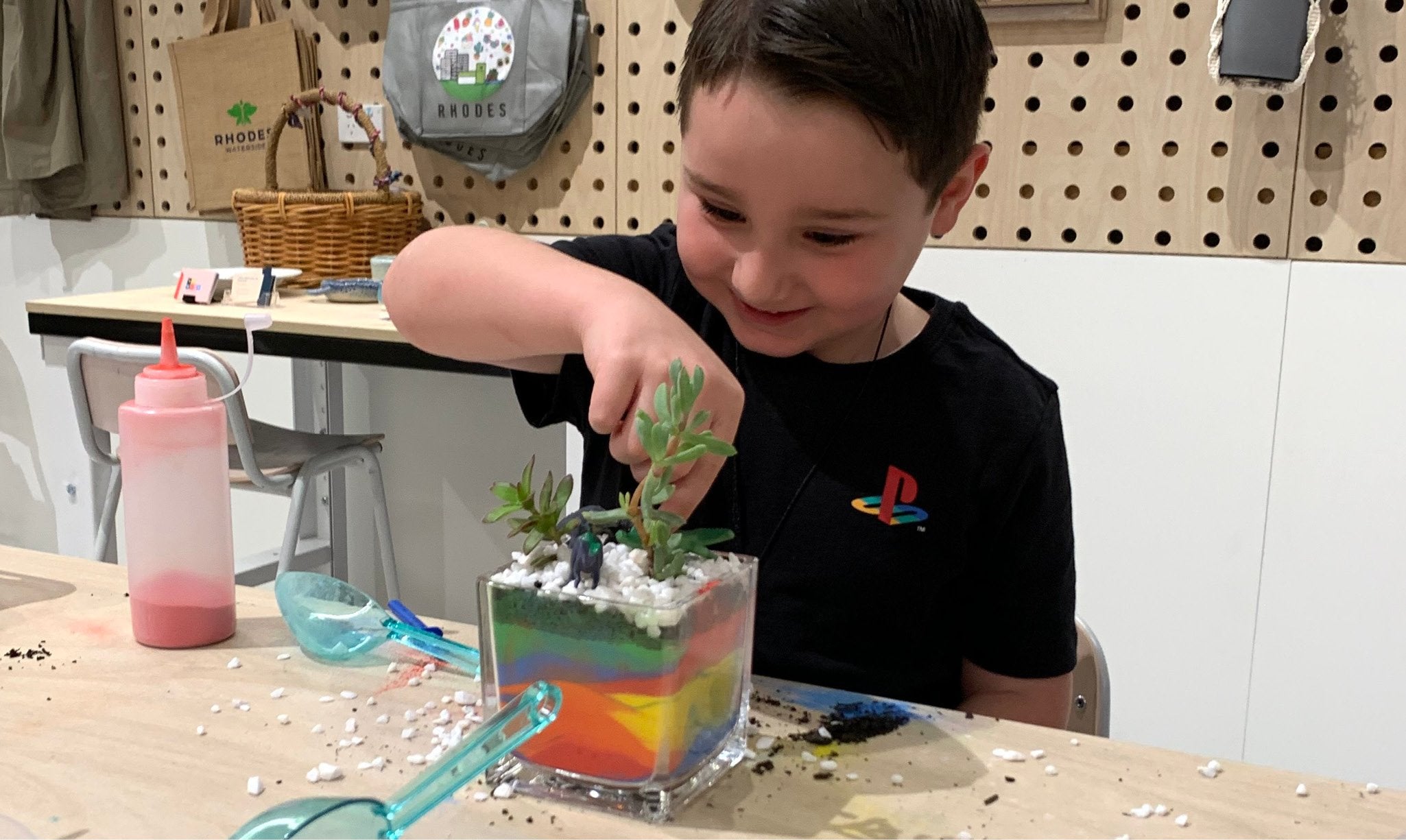 A child building a terrarium with succulents and colour sand.